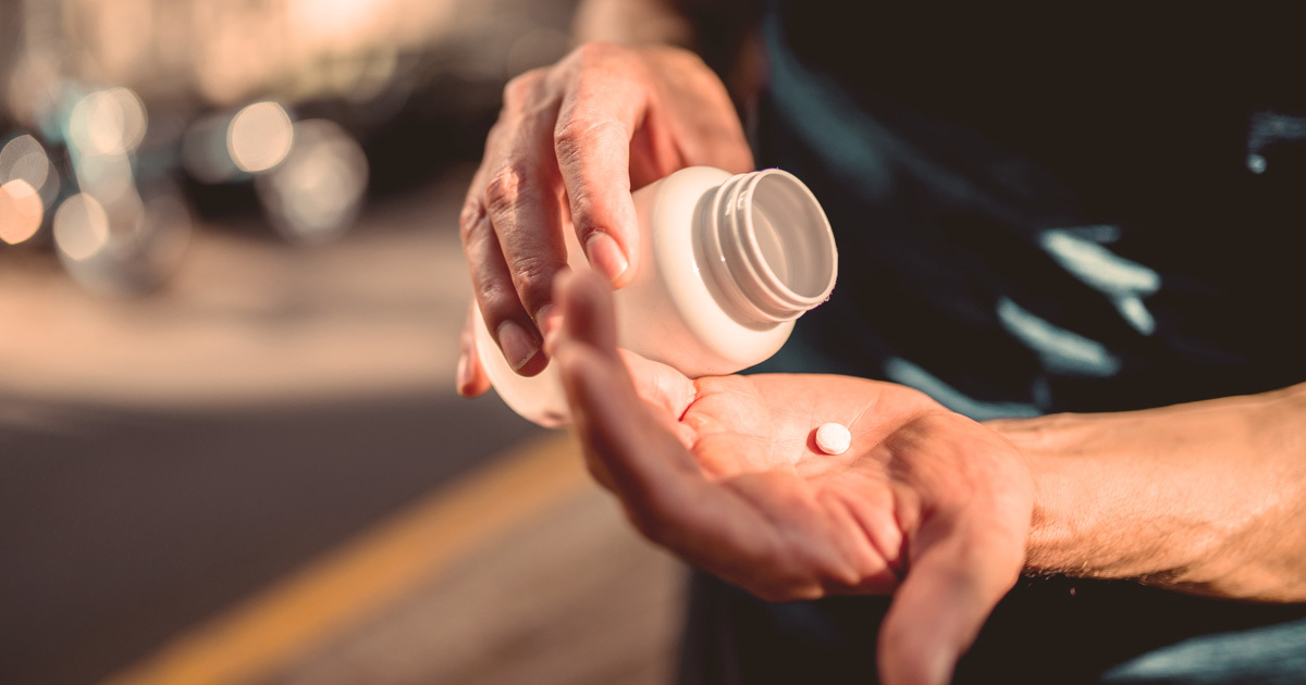A person holding a medicine bottle and a pill